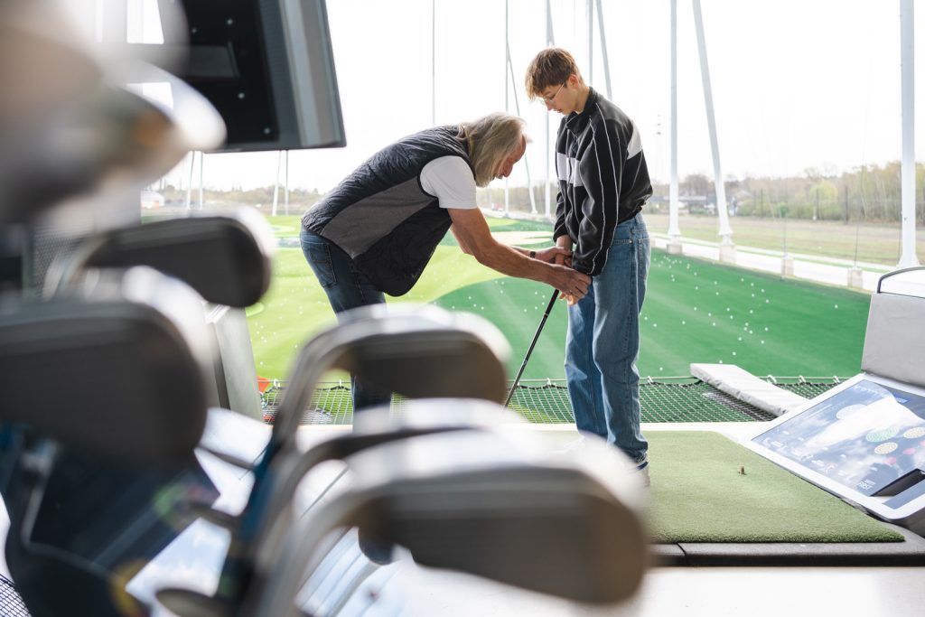 Jeune golfeur qui reçoit les conseils d’un coach sur la bonne position à prendre avant de s’élancer.