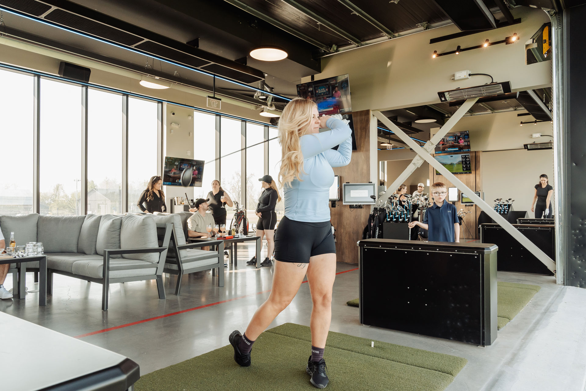 Golfeuse effectuant son élan sur un simulateur intérieur moderne, avec un espace salon confortable et de larges fenêtres en arrière-plan chez Super Golf.
